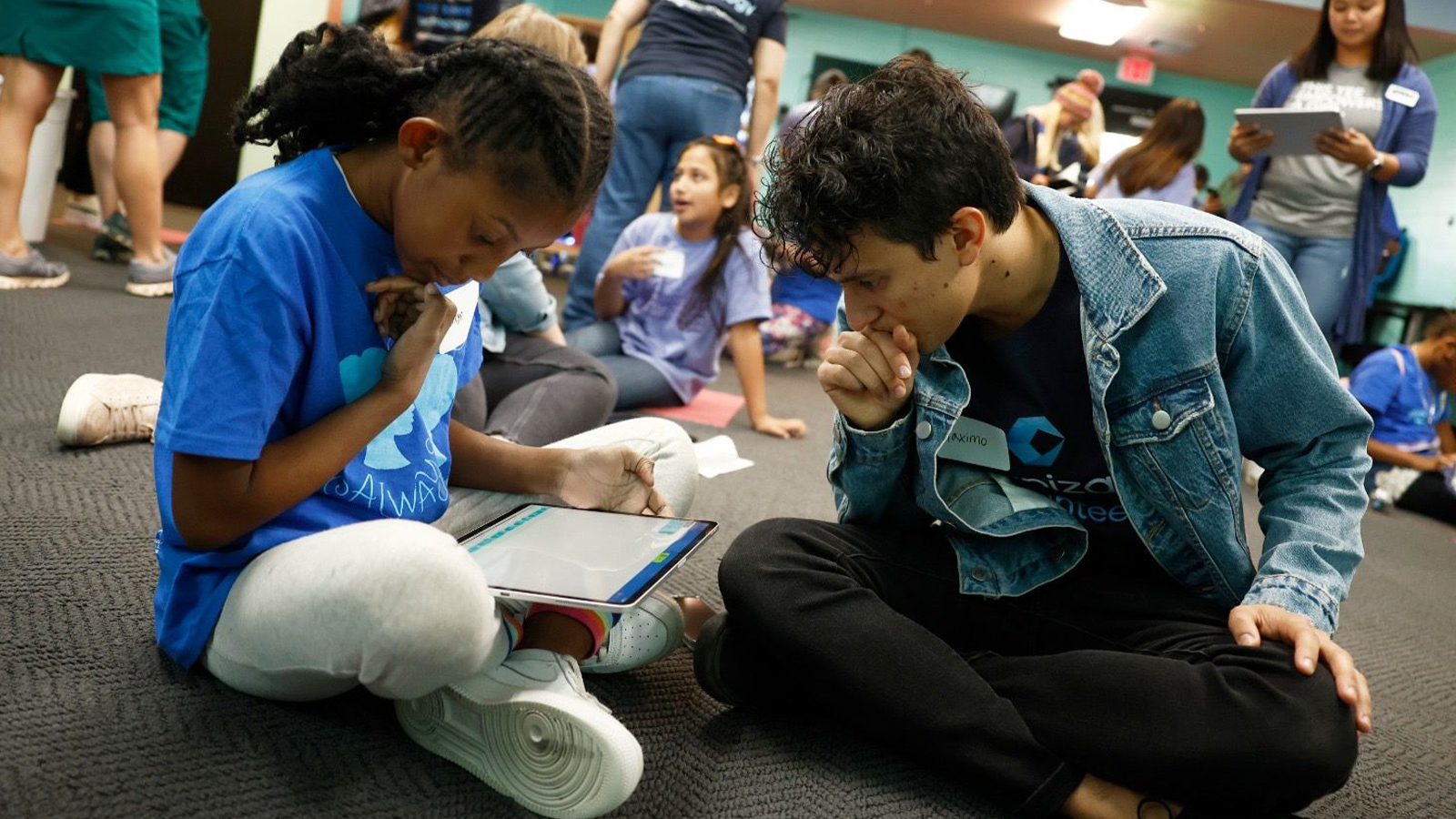 a person and person sitting on the floor looking at a tablet