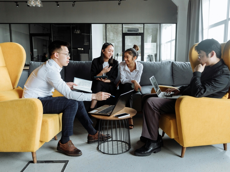 a group of people sitting around a table with laptops